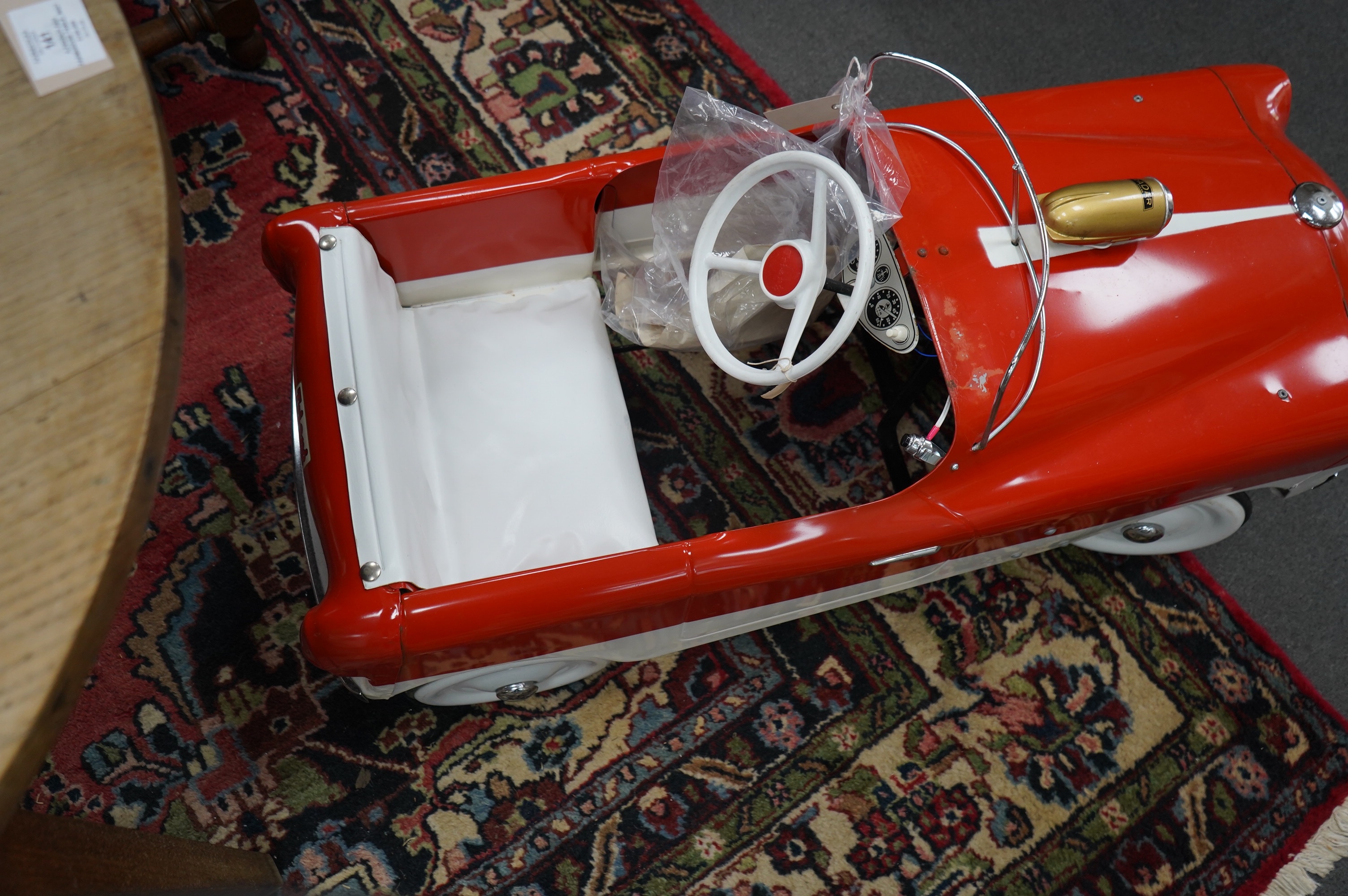 A tinplate Tri-ang T65 pedal car, based on a Ford Zephyr, with vinyl padded seat, working steering, working electric headlights, original paperwork and Radar bicycle horn with original card box, length 98cm. Condition -